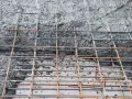 Siatka zbrojeniowa czeka na beton na fundament. Powierzchnia jest szara i chropowata, z widocznymi prętami.