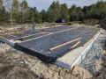 Gotowy fundament pod dom szkieletowy, z czarną folią i drewnianymi belkami, czeka na dalsze prace budowlane.
