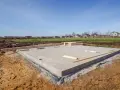 Płyta fundamentowa, jeden z rodzajów fundamentów, gotowa pod budowę domu. W tle domy i błękitne niebo.