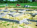 Budowa fundamentu z bloczków betonowych. Dwóch robotników pracuje przy wznoszeniu ścian fundamentowych.
