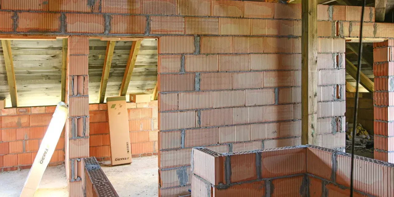 Budowa domu z pustaków ceramicznych. Widać niedokończone ściany, belki stropowe i materiały budowlane. Murowanie na piankę wady mogą pojawić się przy nieprawidłowym wykonaniu.