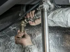 Ręce majstra dokręcają złączkę podczas próby szczelności instalacji c.o. zgodnie z normą.