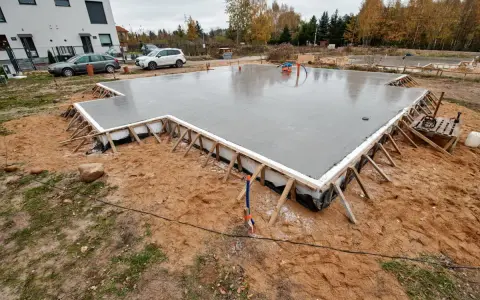 Świeżo wylany beton na budowie. To solidne, najtańsze fundamenty pod przyszły dom, otoczone drewnianym szalunkiem.