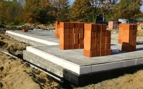 Budowa domu: fundamenty z bloczków betonowych, płyta fundamentowa i stosy pustaków ceramicznych.