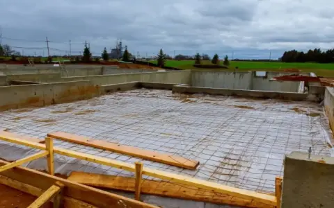Fundament budowlany z zbrojeniem, przygotowany pod wylanie betonu. Widać betonowe ściany fundamentowe i siatkę stalową na podłożu.