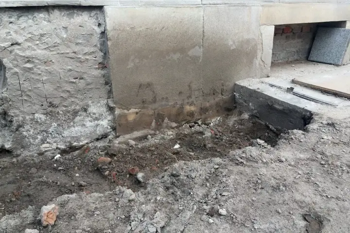 Odsłonięty fundament z cegły, ziemia i gruz wokół. Trwa remont.